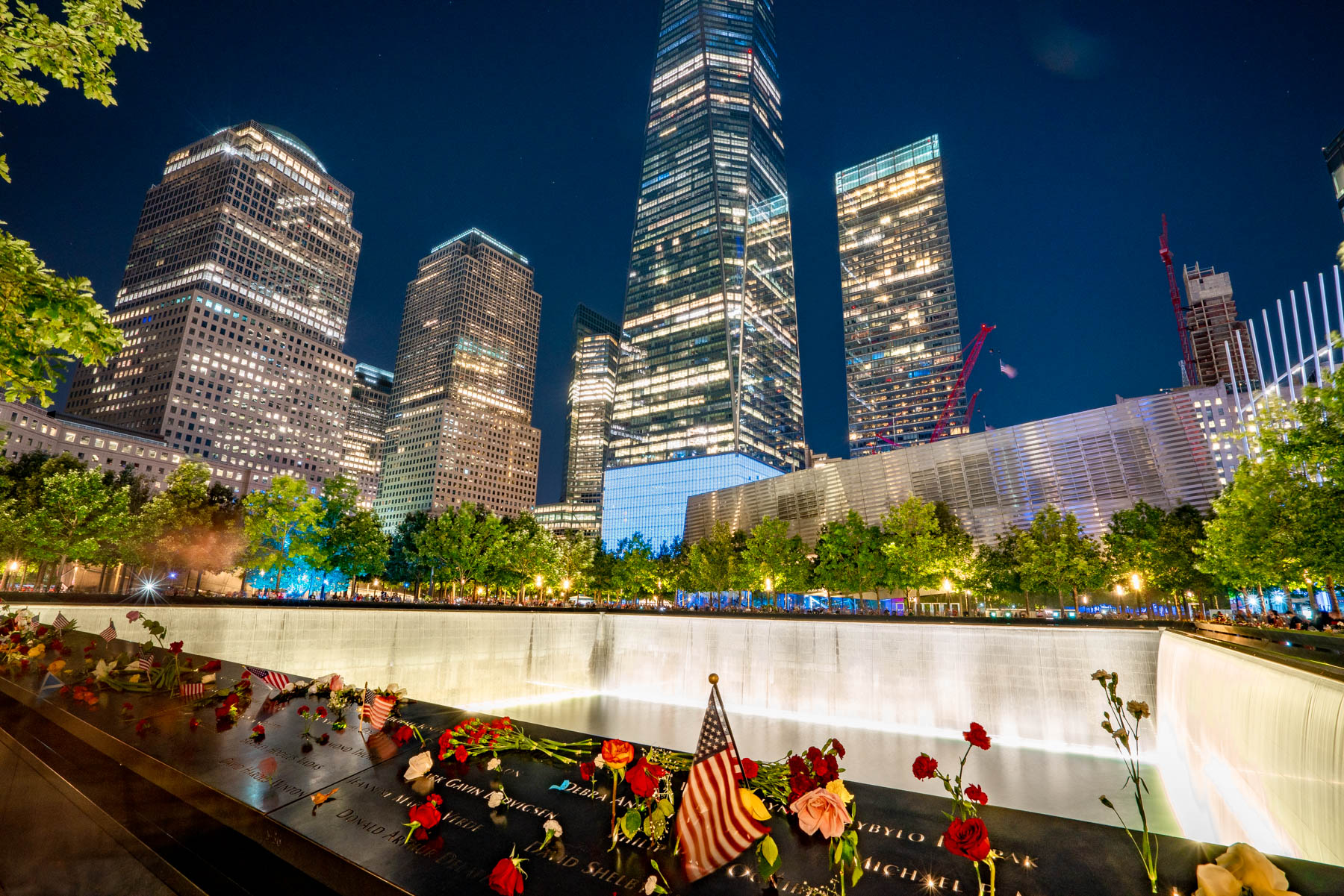 Flowers and flags left in remembrance of the Twin Tower attacks at the 9/11 Memorial Site in the Financial District at night