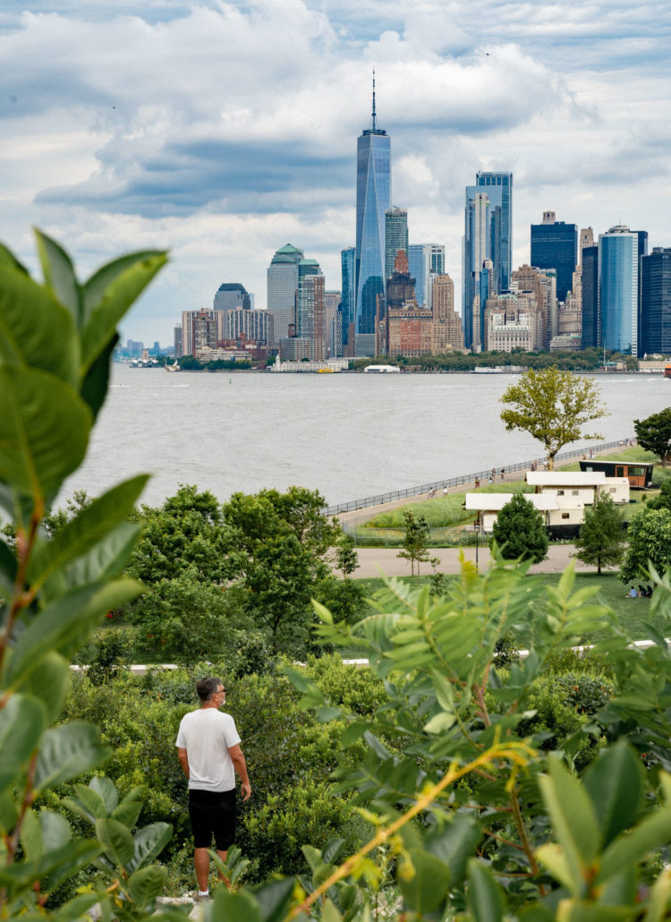 A man in a white shirt standing at an outlook full of greenery enjoying one of the best things to do on Governors Island, enjoying the view