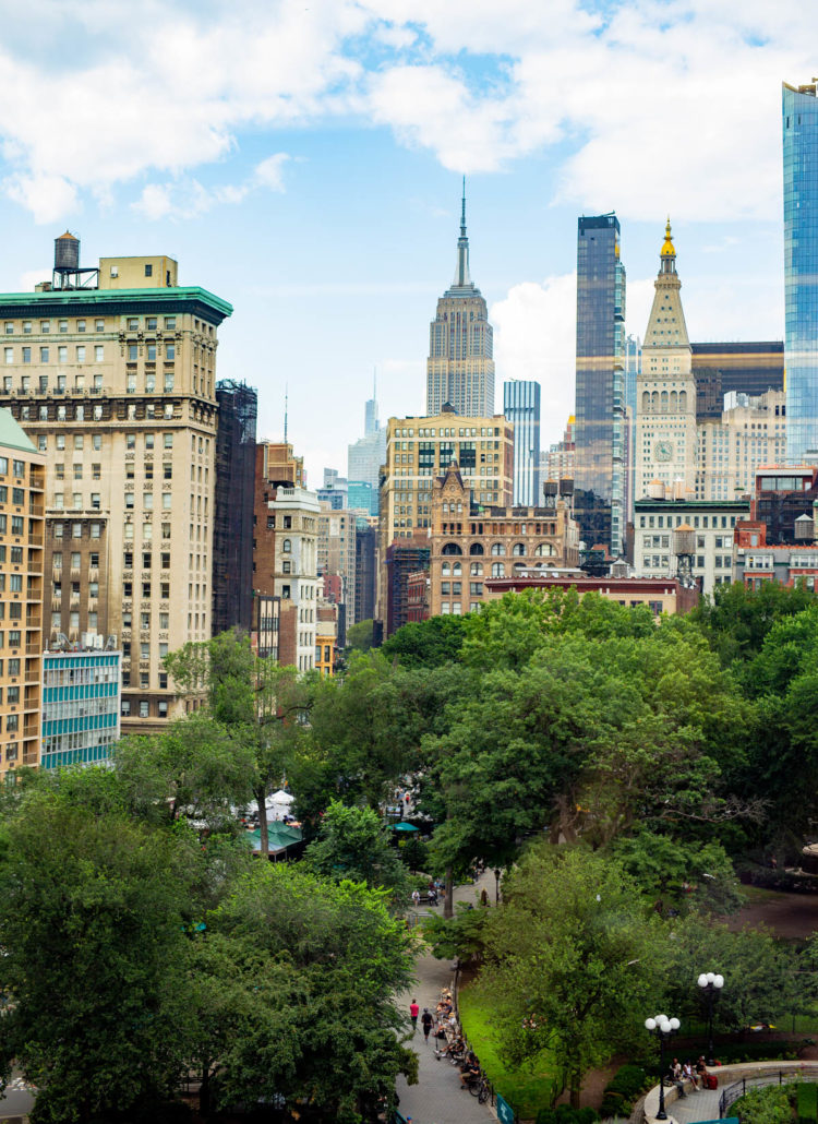 People enjoying one of the best things to do in Union Square by soaking up the Views of the Empire State Building and Union Square Park in Summer swarmed by greenery
