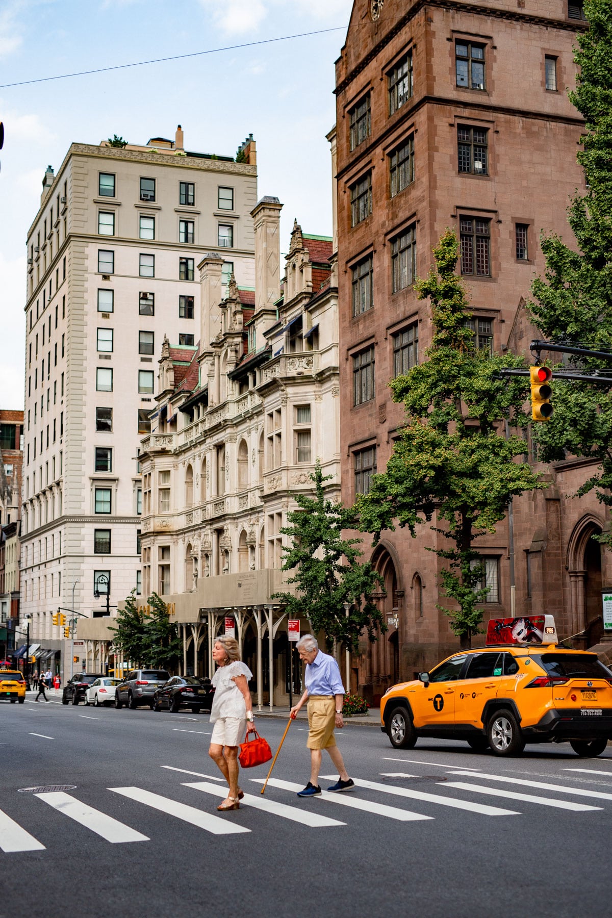 A woman with a red purse and a man with a cane are crossing the street with a taxi driving behind them in the Upper East Side, one of the best neighborhoods to live in NYC