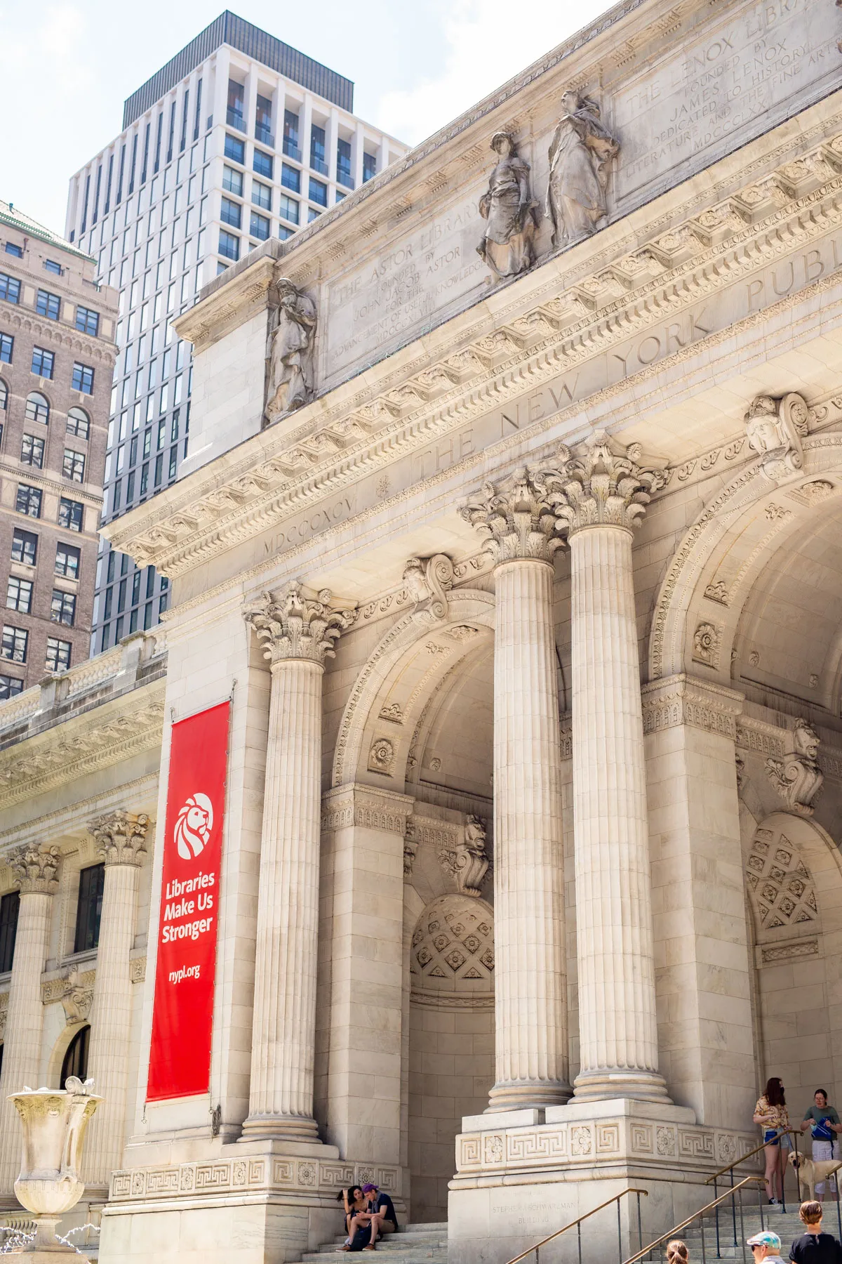 People sitting on the steps of the New York Public Library with a red banner that says "Libraries make us stronger", Marble architecture 