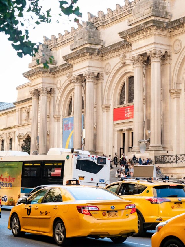 Multiple taxis driving on a busy street in front of the Metropolitan Museum of Art, one of more than 80 museums in NYC
