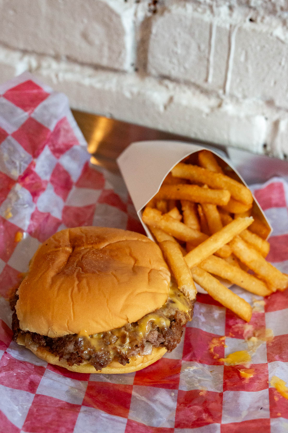 Smash cheeseburger from 7th Street burger with crispy fries on a checkered red and white wrapper