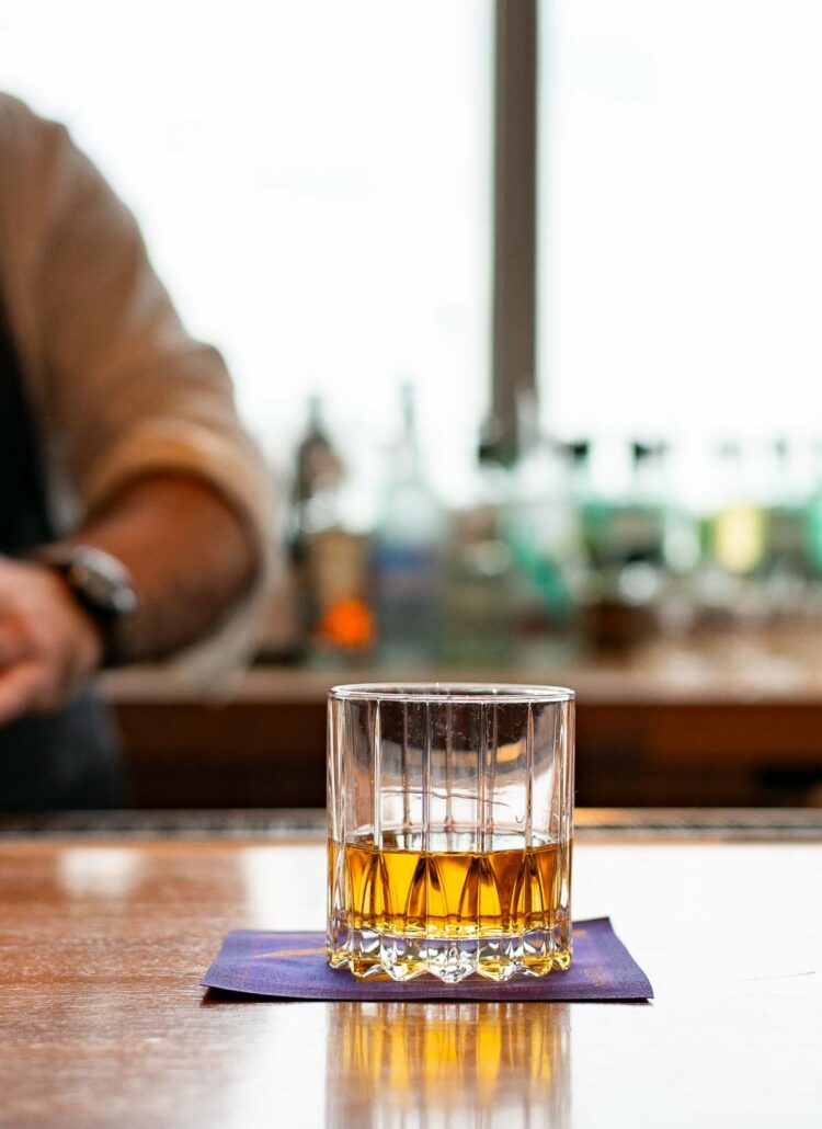 a glass of whiskey on a purple napkin from Manhatta, one of the best rooftop bars in Manhattan
