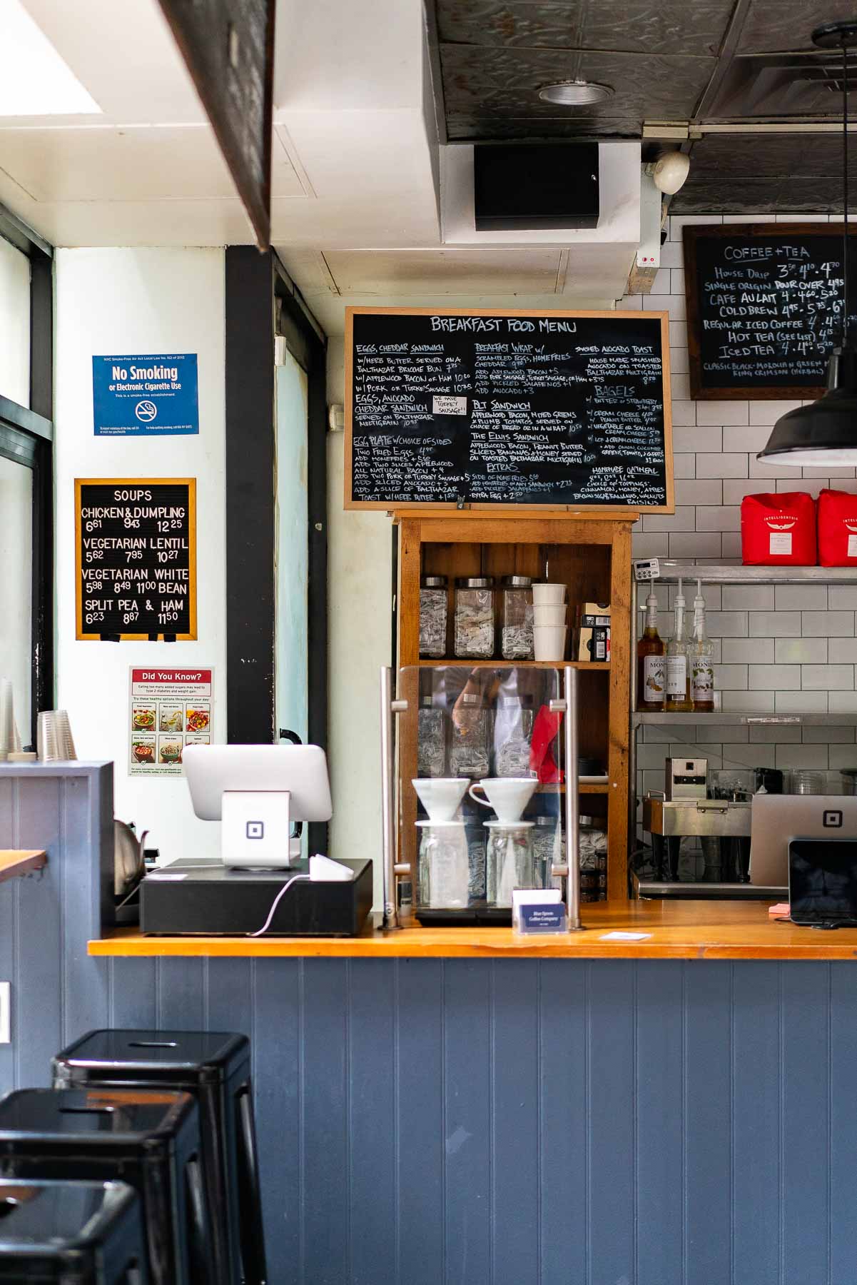 An empty ordering counter that's dark blue and has a wooden countertop at Blue Spoon Coffee, surrounded by coffee-making tools and menus