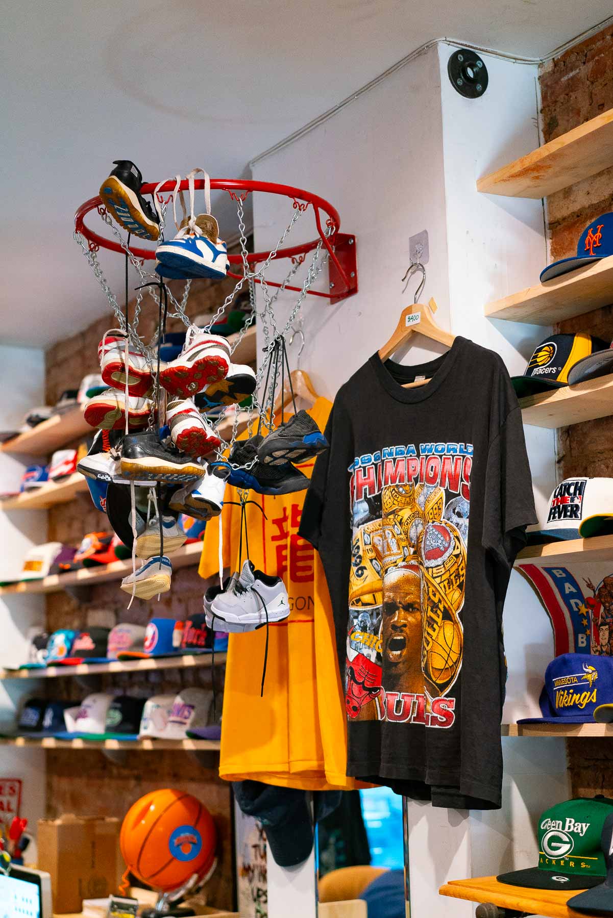 Baby-sized Jordans (shoes) hanging off a basketball rim attached to the wall with basketball-themed t-shirts and shelves full of hats at Mr. Throwback, one of the best vintage stores in New York City
