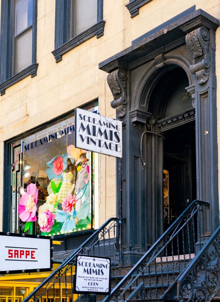 Entrance stairs and doorway to Screaming Mimi's Vintage, with a colorful display of clothing and flowers in its window, one of the best thrift stores in NYC