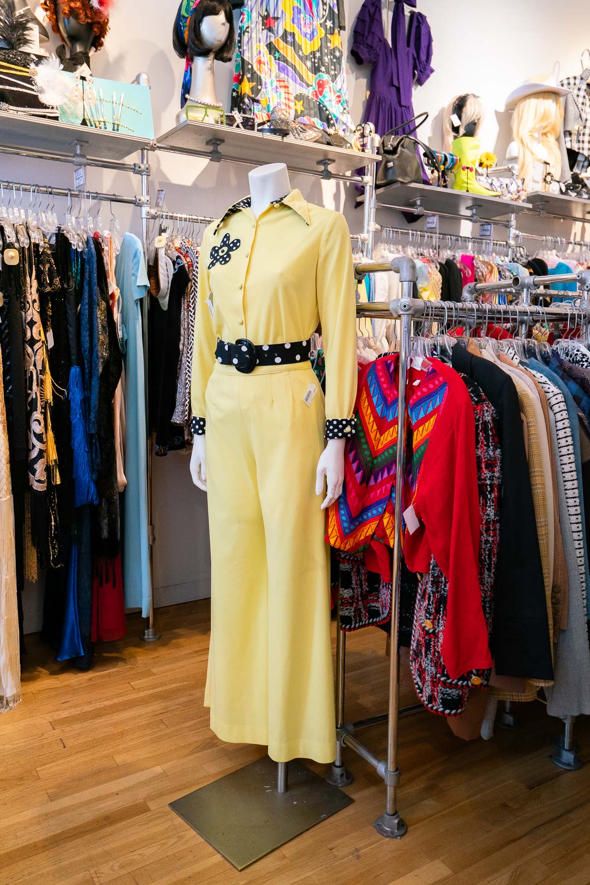 A yellow outfit with black belt on a mannequin at Screaming Mimi's Vintage, with clothing racks behind it