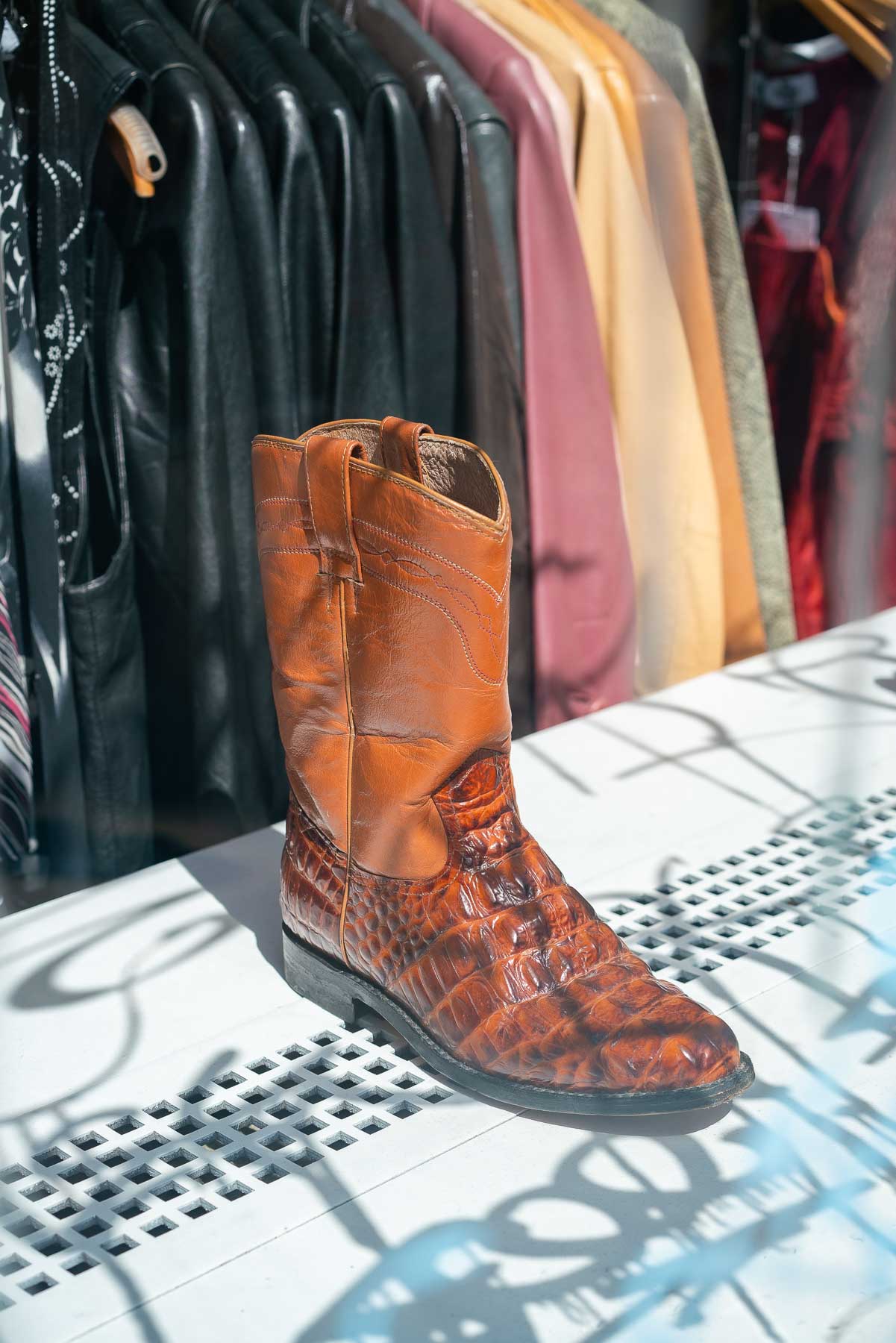 Cowboy boot on display behind a window at the Vintage Twin in the Lower East Side, with a rack of jackets behind it. The Vintage Twin is one of the best thrift stores in New York City